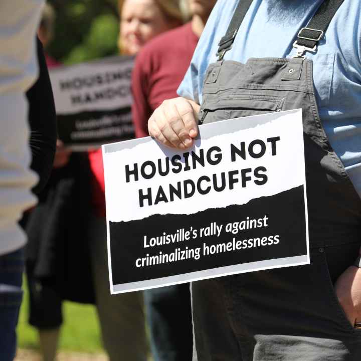 A person holds a sign that says "Housing Not Handcuffs, Louisville's Rally Against Criminalizing Houselessness"